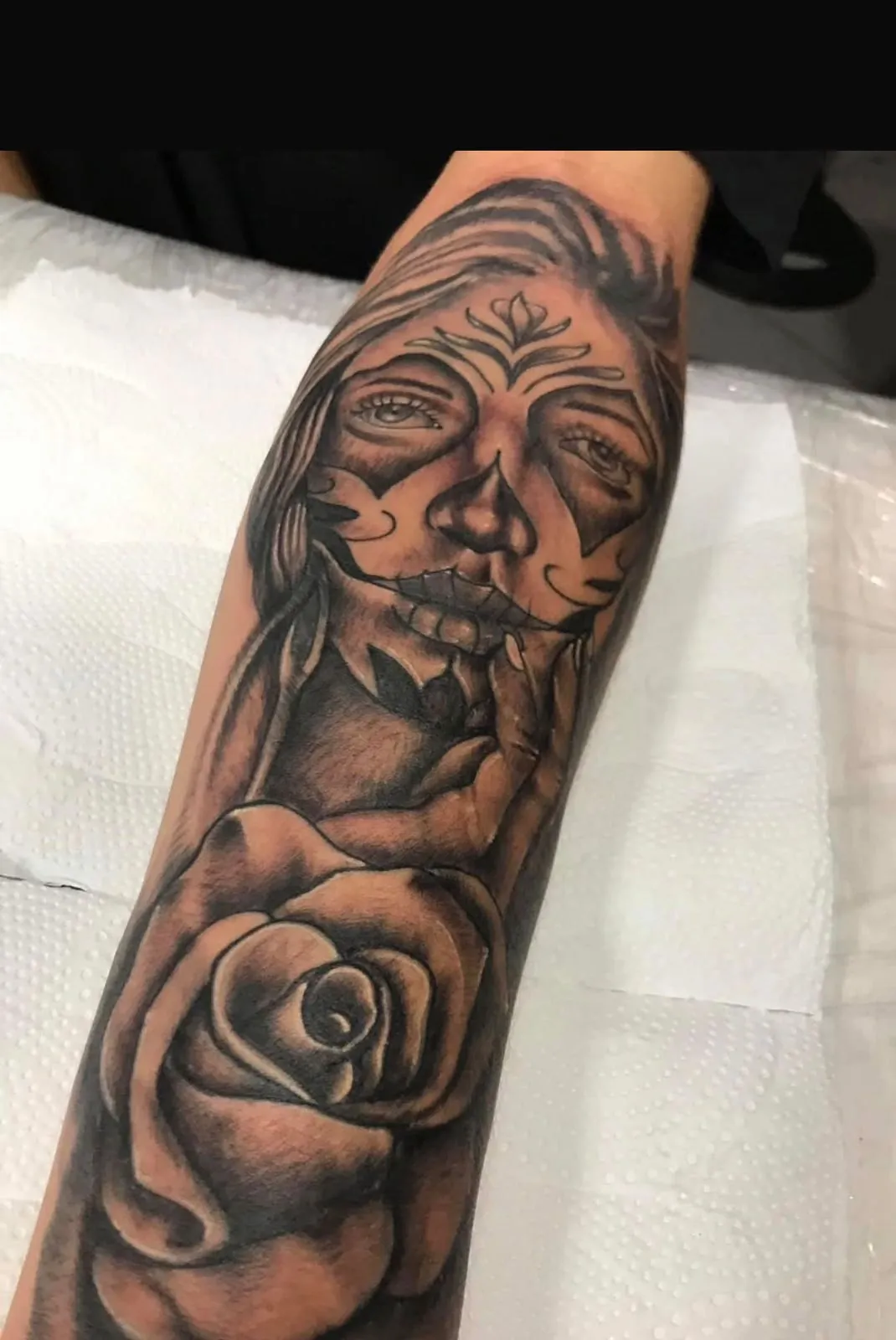 Tatuagem realismo preto e cinza de catrina com rosa no antebraço